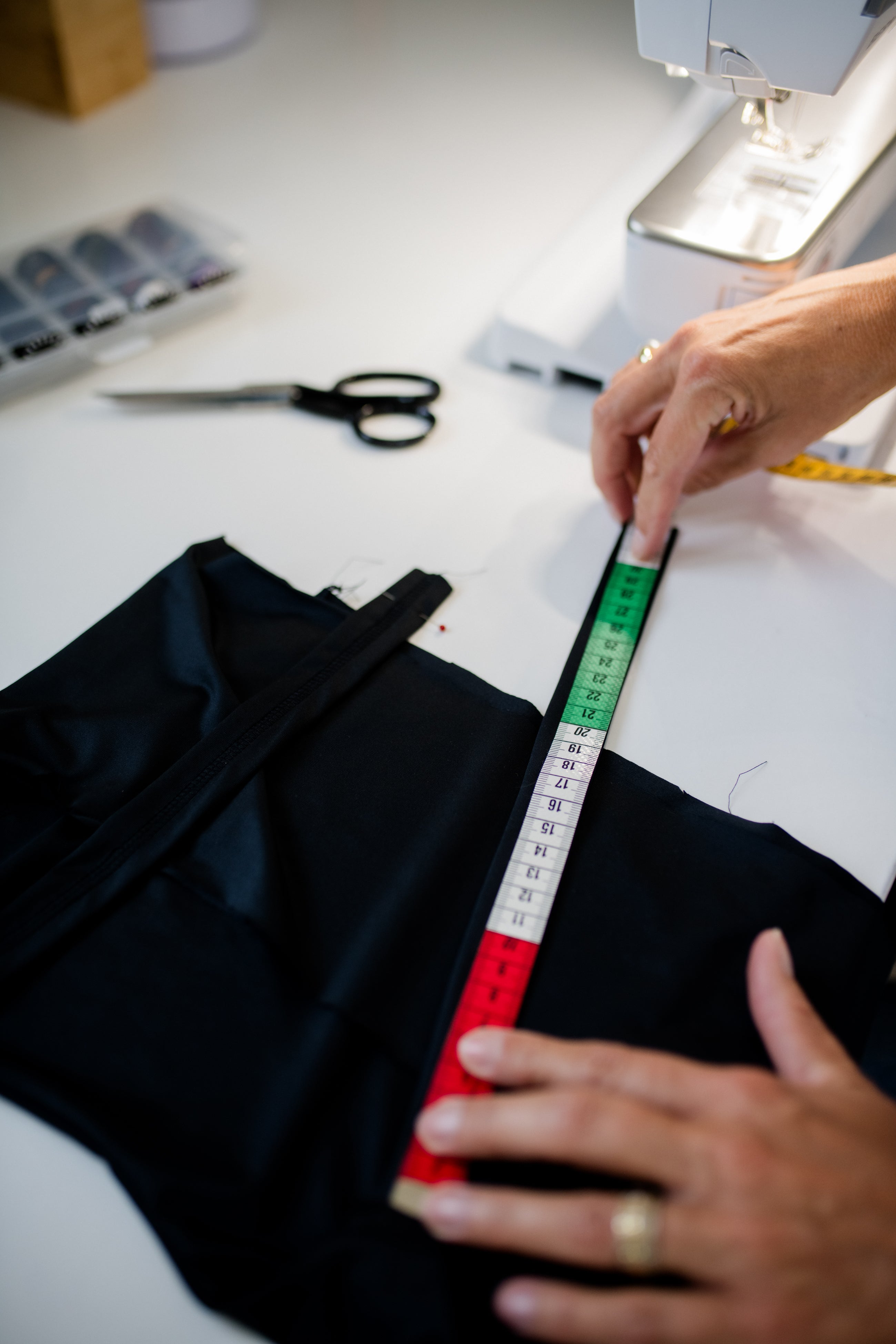 Ausmessen des Jumpsuit Oberteiles. Hände mit italienischem Lineal an schwarzem Material.