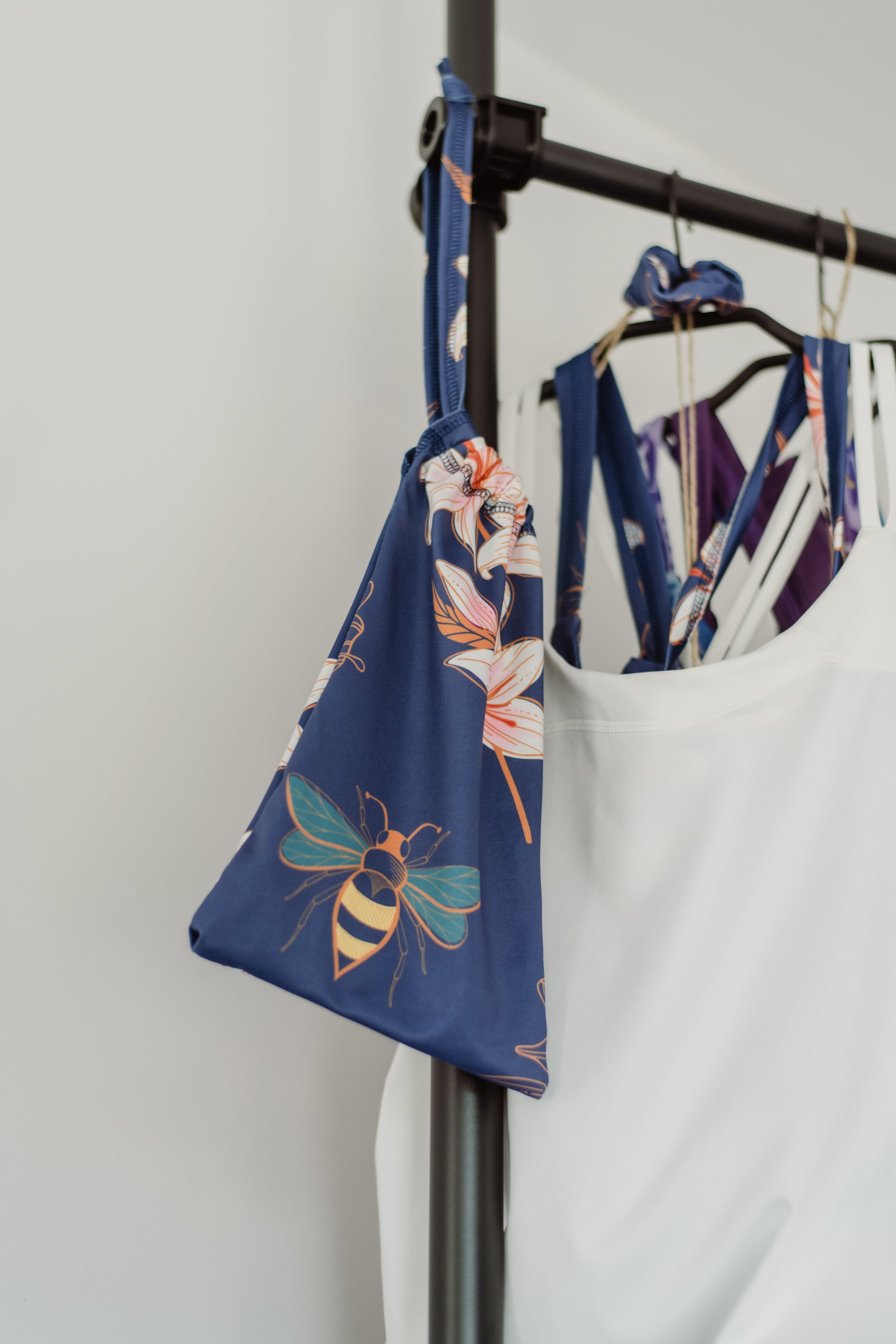 Blauer Stoffbeutel für die Verpackung des Jumpsuit an einer Stange. Biene auf Stoff mit Blumenmuster.