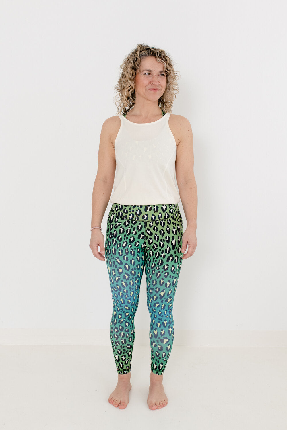 Yoga Jumpsuit mit hellem Oberteil und Leopardenmuster Unterteil in grün an Blondine mit Locken