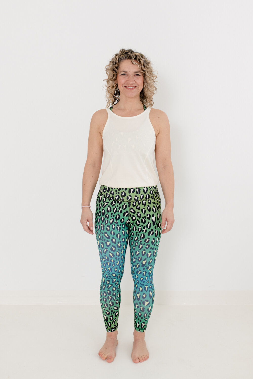 Yoga Jumpsuit mit hellem Oberteil und Leopardenmuster Unterteil in grün an Blondine mit Locken