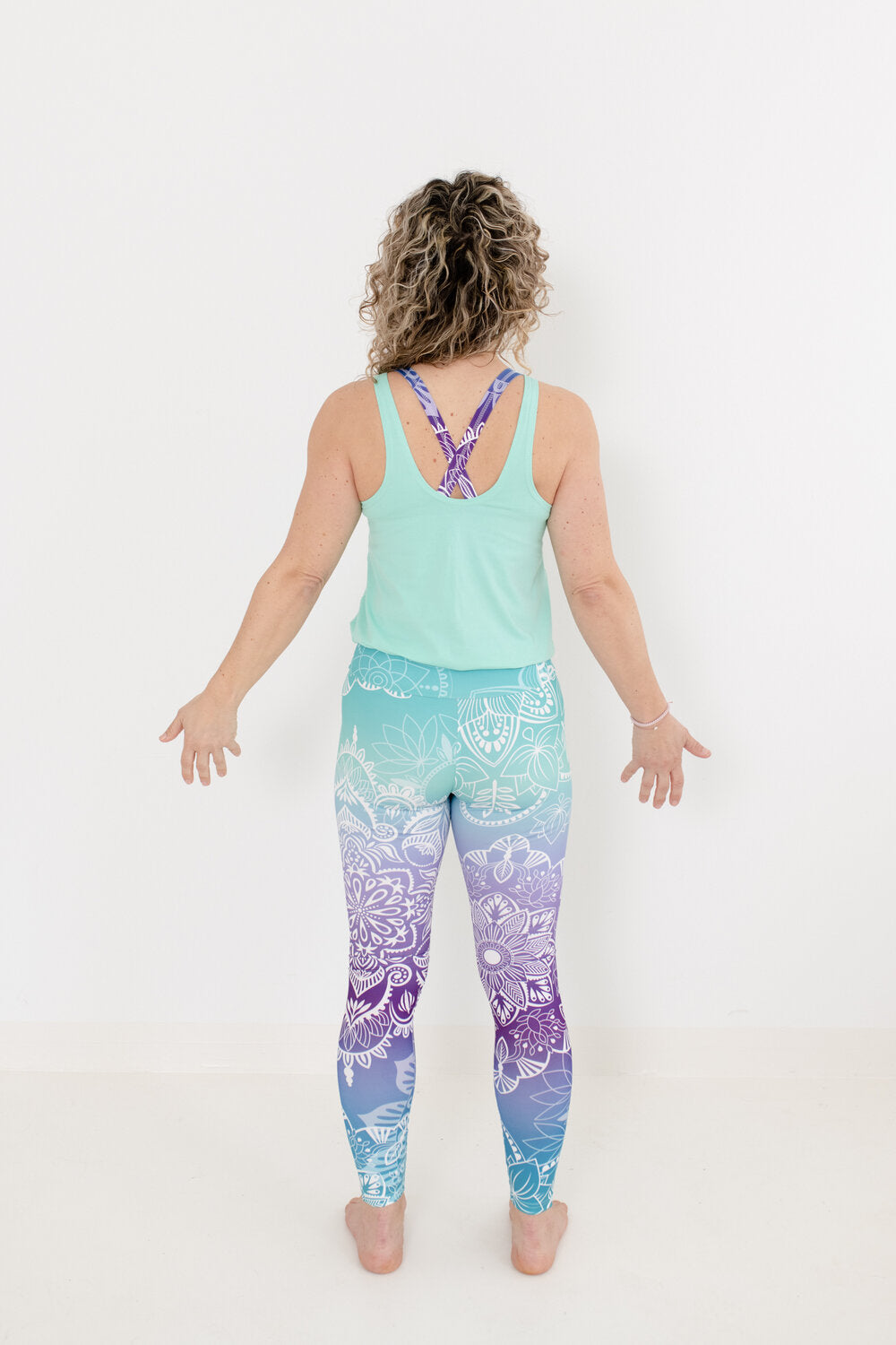 Yoga Jumpsuit mit türkisem Oberteil und Meer-farbendem Unterteil mit Muster an Blondine mit Locken