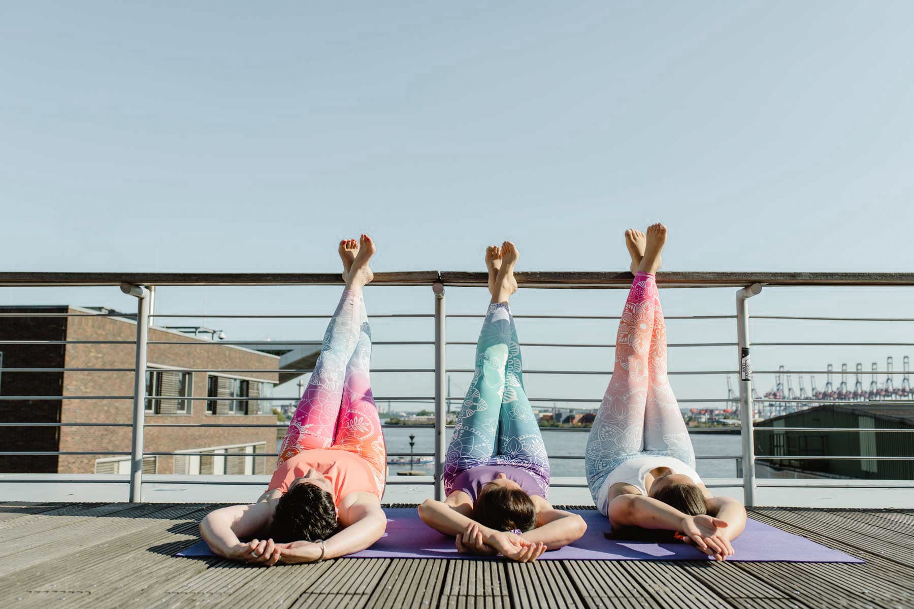 Drei Frauen mit bunten farbigen und ästhetischen Yoga Jumpsuit in entspannter Pose mit Beinen in der Luft