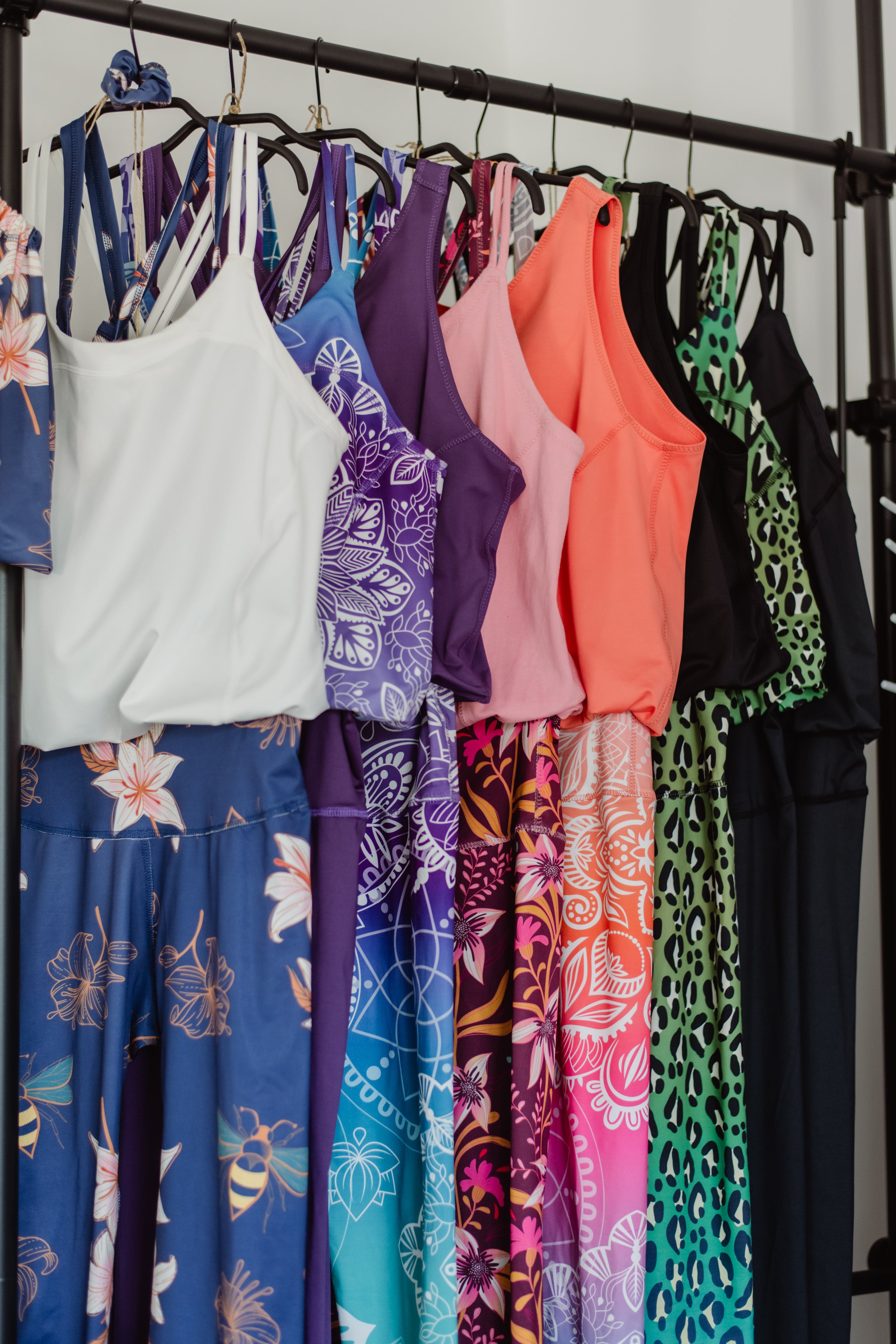 Yoga Jumpsuit Kollektion aus unterschiedlichen Mustern. Unterschiedlich farbige Yoga Jumpsuits auf der Stange. Blumenmuster, Leomuster, einfarbig.