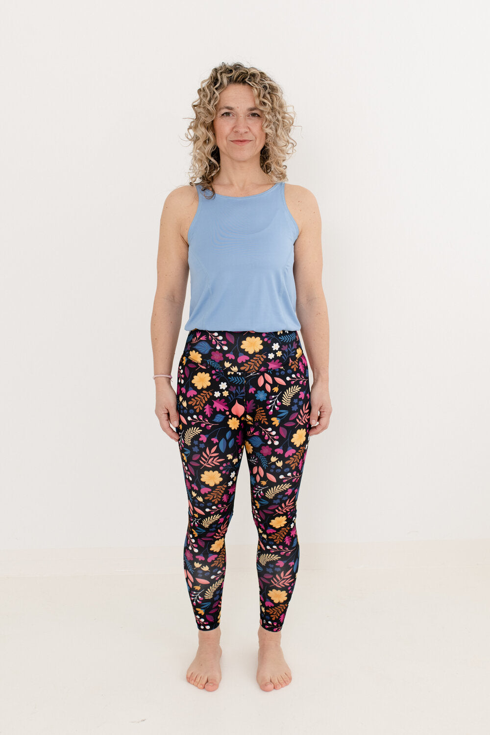 Blondine mit Locken trägt YogaJumpsuit mit hellblauem Oberteil und Blumenmuster unterteil