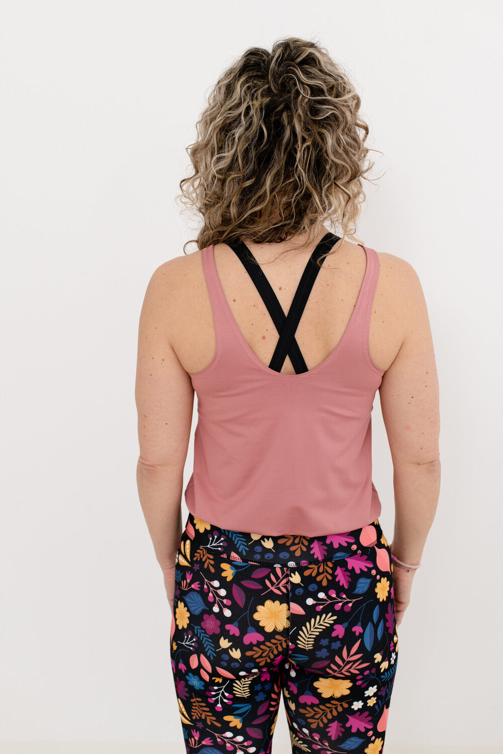 Von hinten fotografierte Frau, welche einen altrosa-Blumenmuster Yoga Jumspuit trägt